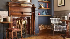 A cozy room with a fireplace, a plaid armchair, and a wooden table. - The Cedars Inn by Greene King Inns (Barnstaple)