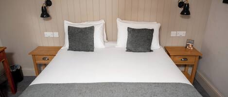 Una cama bien tendida con dos almohadas, una mesita de noche con una lámpara y una pared con papel tapiz floral.