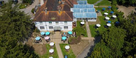 An aerial view of a hotel with a large garden, outdoor seating area, and a parking lot.
