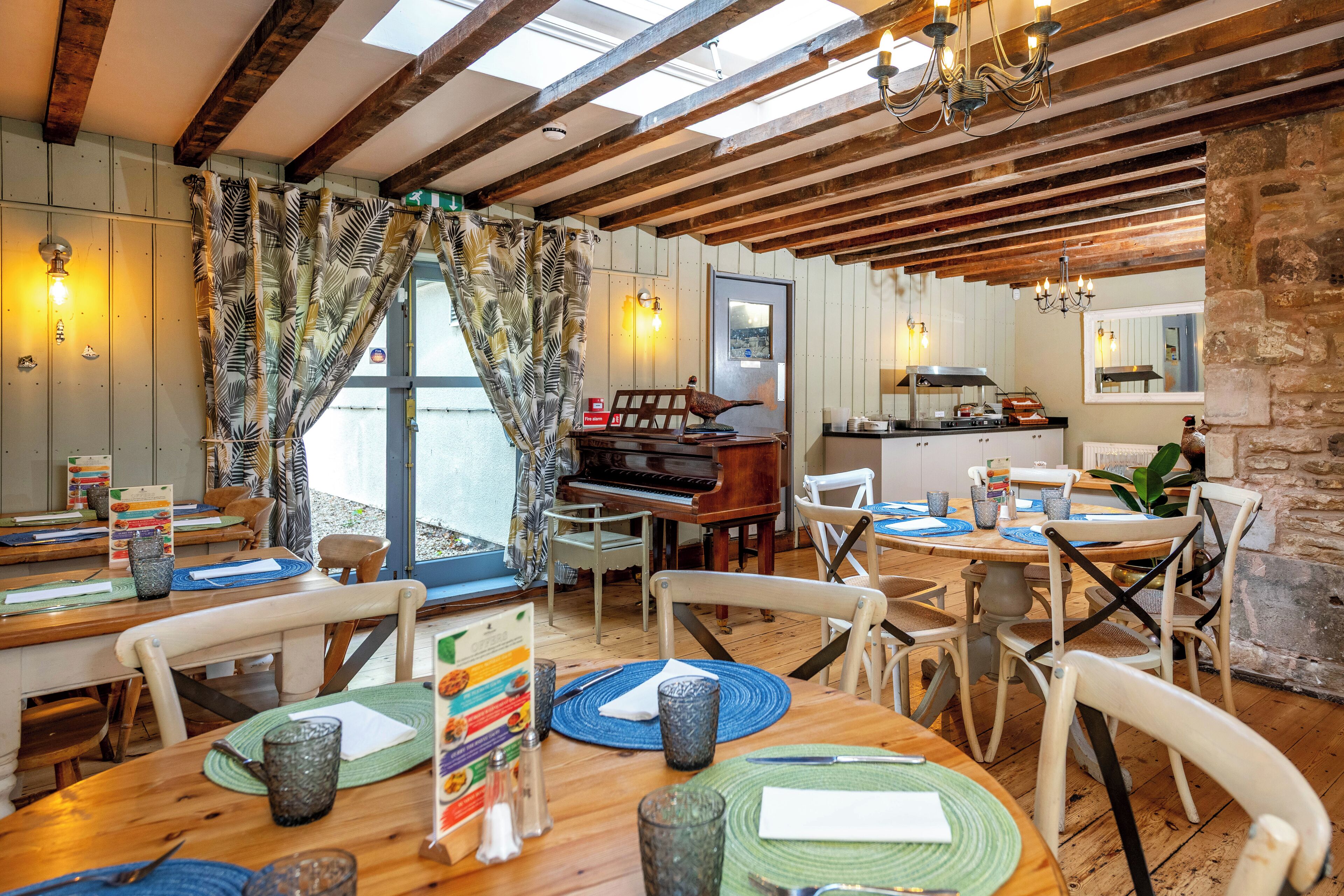 A dining area with wooden tables, chairs, and a piano.
