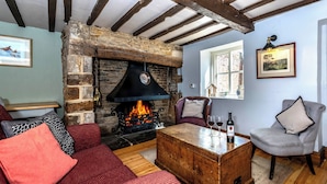 Un salon chaleureux avec une cheminée en pierre, des canapés rouges et gris, une table basse en bois et une fenêtre donnant sur un mur de briques.