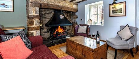 Una sala de estar acogedora con chimenea de piedra, sofás rojos y grises, una mesa de centro de madera y un ventanal con vista a un muro de ladrillo.