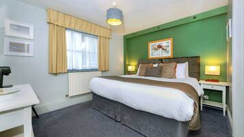 Une chambre d’hôtel avec un grand lit, un bureau, un radiateur et une fenêtre avec des rideaux.