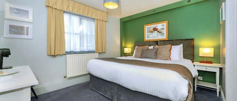 Une chambre d’hôtel avec un grand lit, un bureau, un radiateur et une fenêtre avec des rideaux.