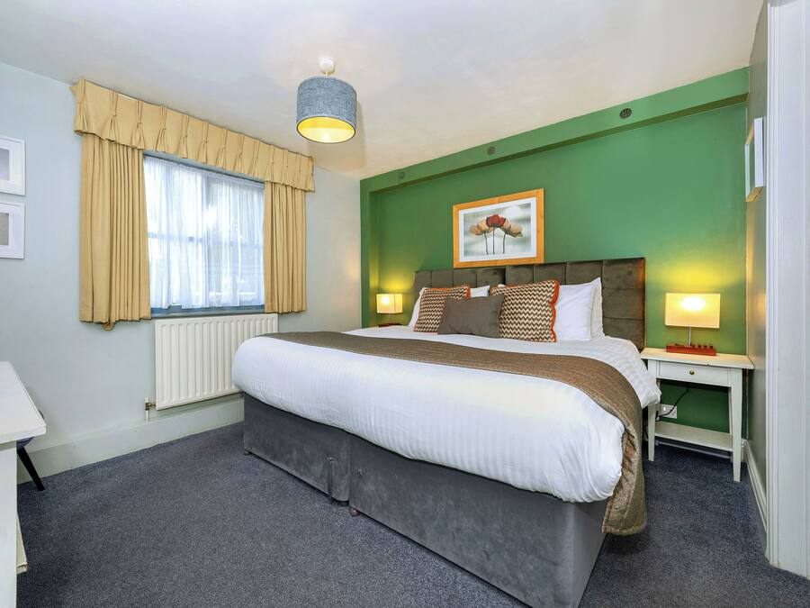 Une chambre d’hôtel avec un grand lit, un bureau, un radiateur et une fenêtre avec des rideaux.