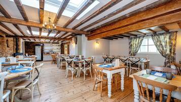 A spacious dining area with wooden tables and chairs, a high ceiling with exposed beams, and a skylight.