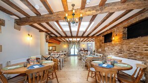 Un coin repas rustique avec des tables et des chaises en bois, des murs en pierre et un lustre.