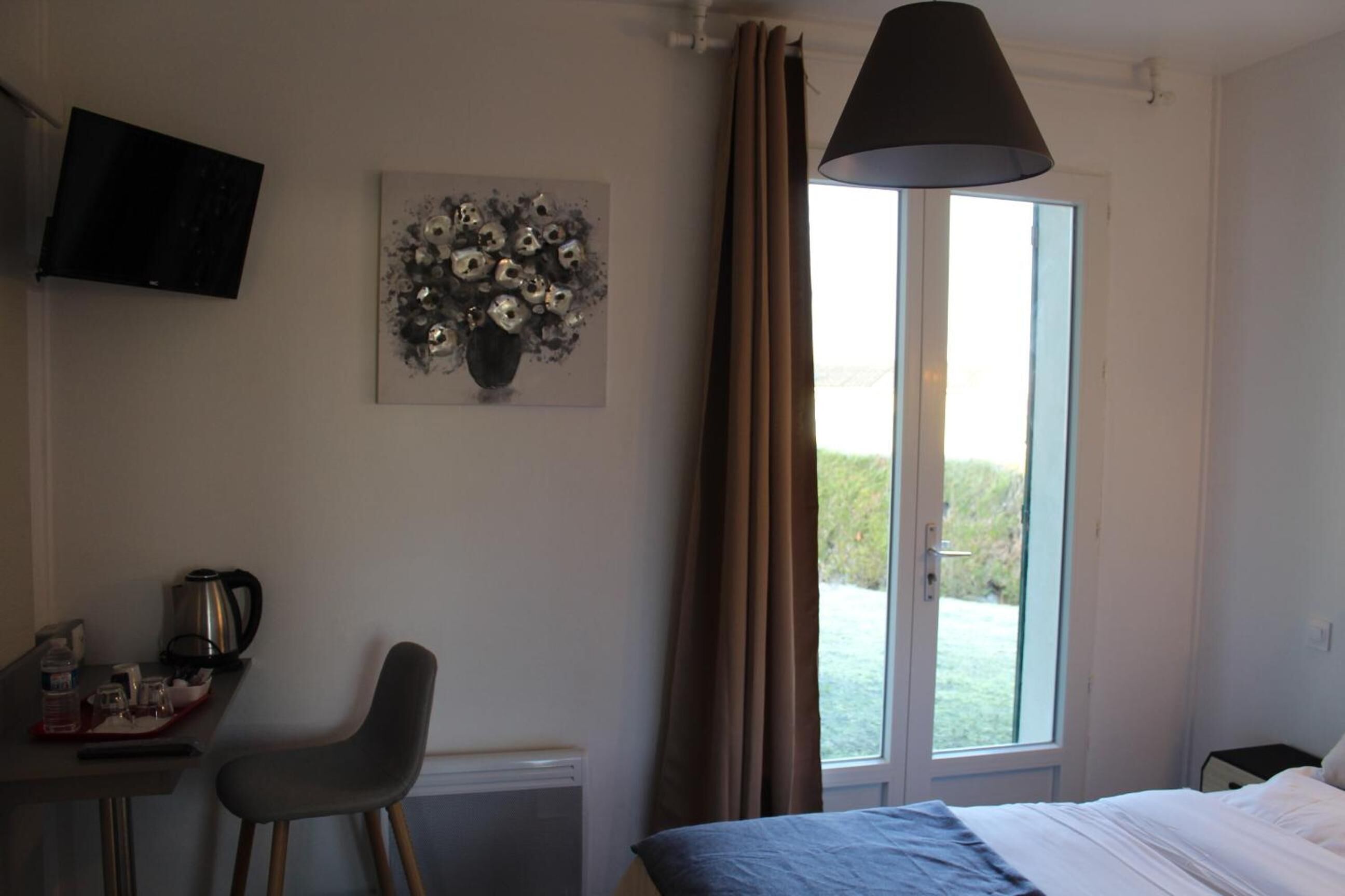 Un dormitorio con cama, escritorio y silla, televisor montado en la pared y ventana con cortinas.
