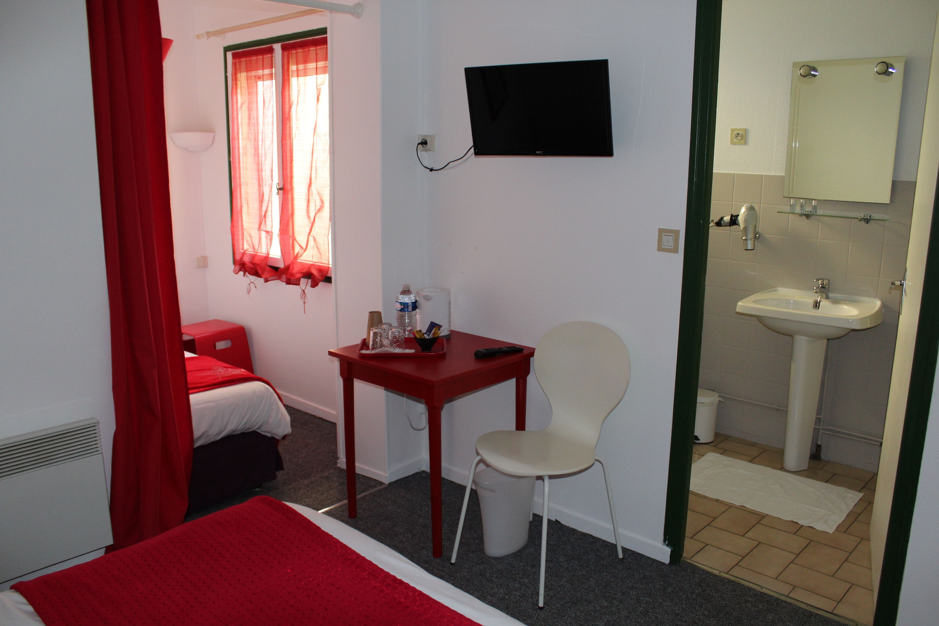 A hotel room with a bed, a desk with a chair, a television, and a bathroom with a sink and mirror.