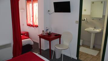 A hotel room with a bed, a desk with a chair, a television, and a bathroom with a sink and mirror.