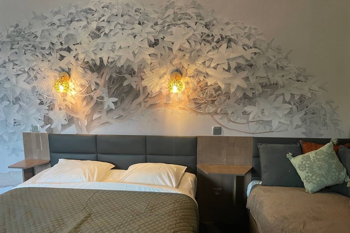Un dormitorio con una cama grande, dos mesitas de noche y una mesita auxiliar, además de una pared con un diseño de hojas.