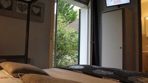 Un dormitorio con cama, ventana con vistas a follaje, una puerta y una pared decorada con corazones.