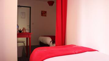 Una camera da letto con un letto, una tenda rossa, una scrivania con una sedia e un tavolino con una bottiglia e una tazza.