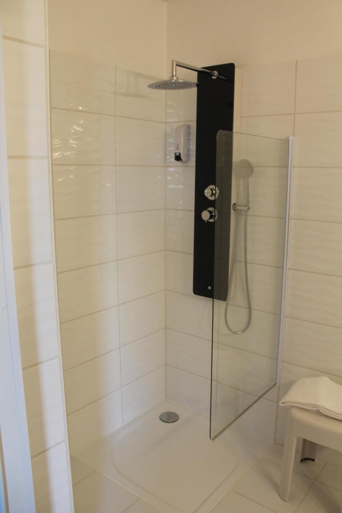 Un área de ducha moderna con cabina de vidrio, cabezal de ducha de mano y panel de control en la pared.