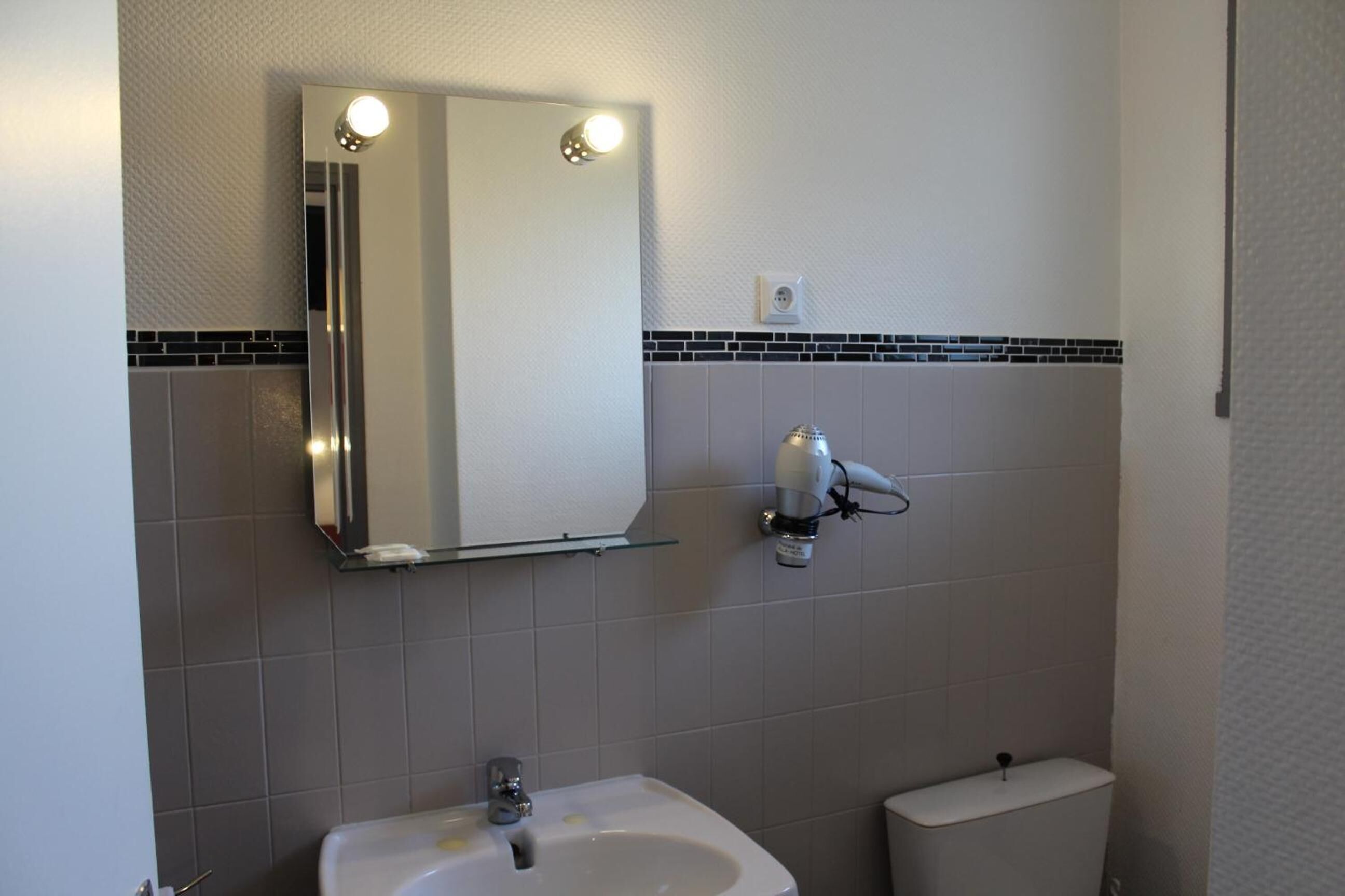 A bathroom with a white sink, a mirror with lights, a towel rack, and a toilet.