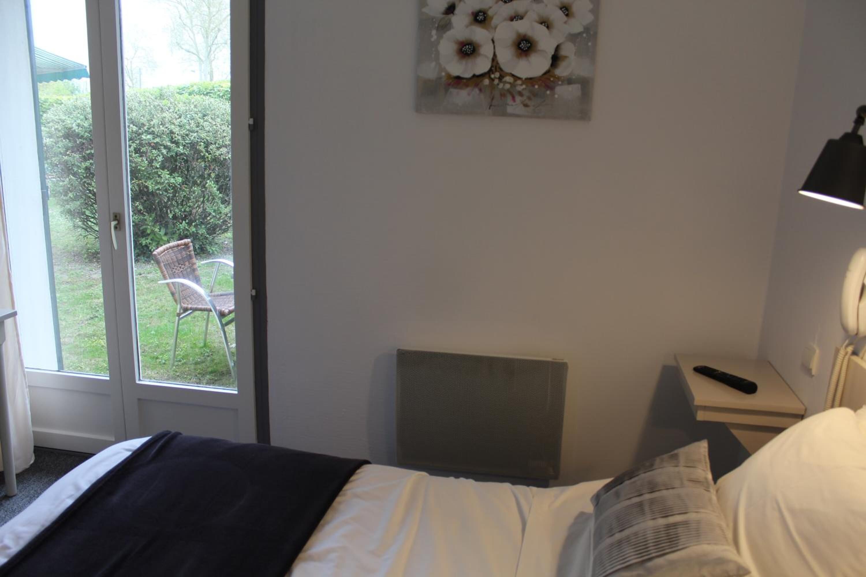 Ein Hotelzimmer mit einem Bett, einem Nachttisch mit Lampe, einem Stuhl vor der Tür und Blick auf den Garten.