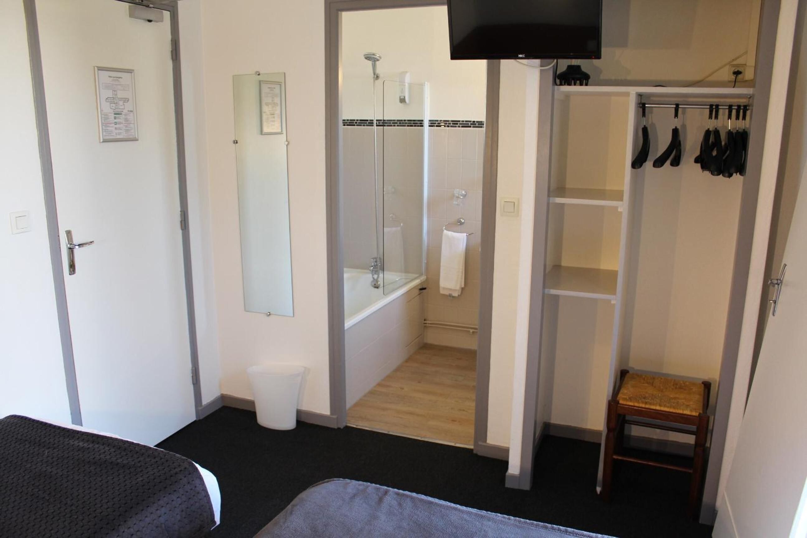 Een hotelkamer met een bed, een badkamer met douche, toilet en een klein houten krukje.