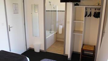 Een hotelkamer met een bed, een badkamer met douche, toilet en een klein houten krukje.