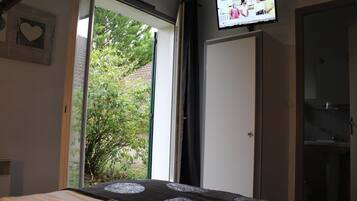 Een slaapkamer met een bed, een aan de muur bevestigde televisie en een raam met uitzicht op groen.