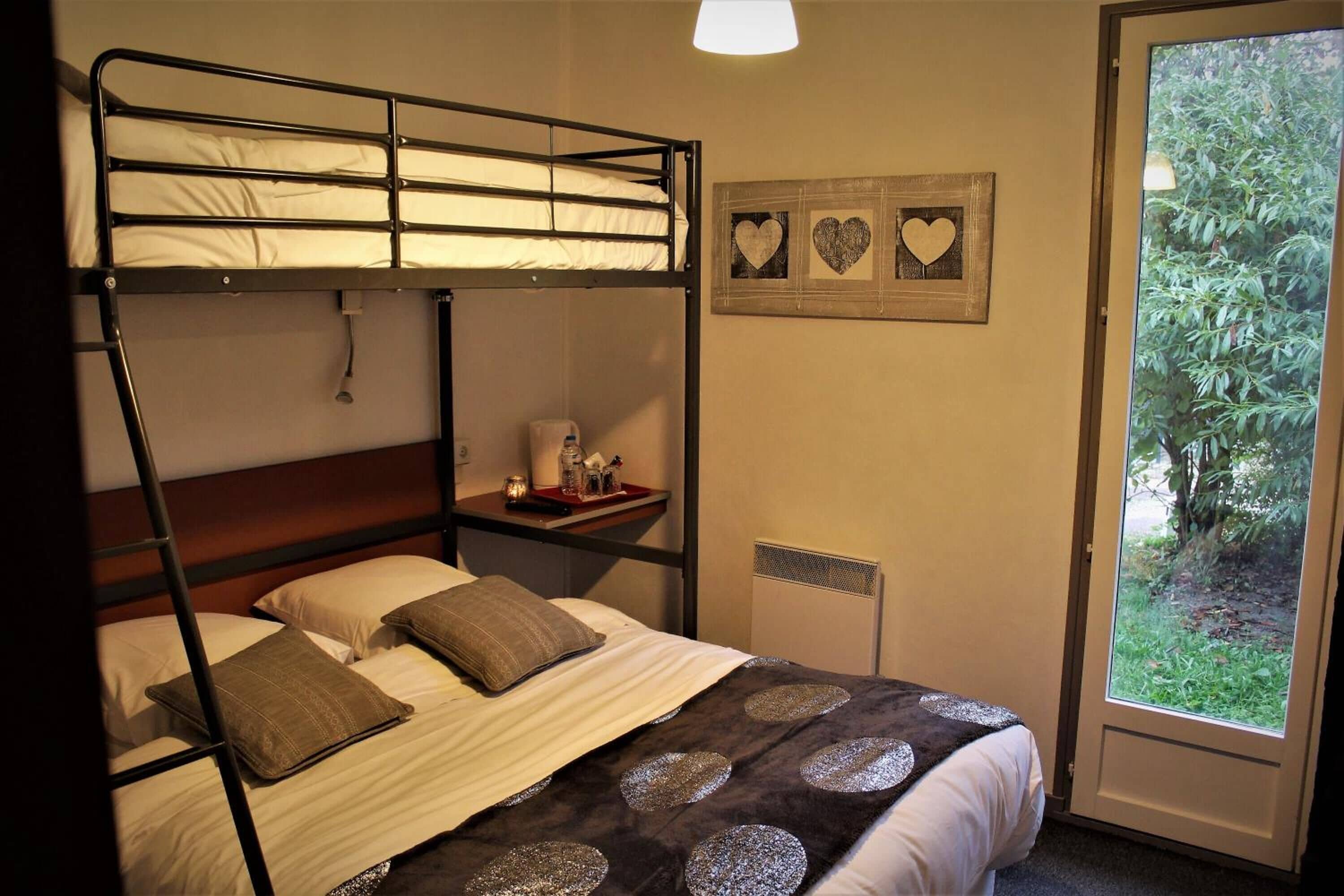 Habitación con literas, vista a la vegetación por la ventana, una mesita de noche con artículos de aseo y un cuadro en la pared.
