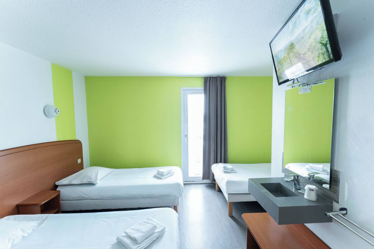 Ein Hotelzimmer mit zwei Betten, einem Badezimmer mit Waschbecken und Spiegel sowie einem an der Wand befestigten Fernseher.
