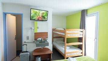 Habitación de hotel con literas, un escritorio con silla, una maleta, un televisor montado en la pared y una ventana con cortinas.