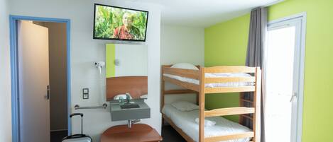 Habitación de hotel con literas, un escritorio con silla, una maleta, un televisor montado en la pared y una ventana con cortinas.