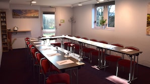 A conference room with a long table, red chairs, a coat rack, and a window with a plant. - Brit Hotel Caen Herouville (Herouville-Saint-Clair)