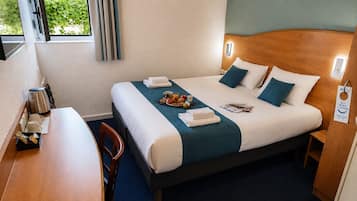 Een hotelkamer met een bed, nachtkastje en een zithoekje.