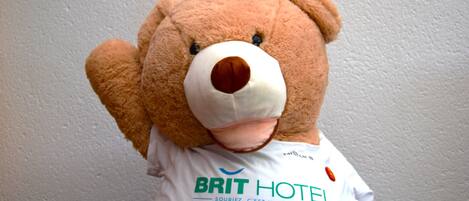 A plush bear wearing a white t-shirt with the text "BRIT HOTEL" and "Souriez, c'est un BRIT HOTEL."