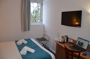 Una habitación de hotel con cama, escritorio, computadora portátil, televisor y ventana con cortinas.