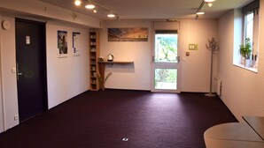 A spacious room with a dark carpet, a door, a shelf with books, a painting, and a window with a view of greenery. - Brit Hotel Caen Herouville (Herouville-Saint-Clair)