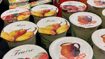 Exhibición de vasos de yogur con motivos de frutas, un letrero que indica 'Producteurs LOCAUX' y una nota sobre 'Yogurt sur le fruit'.