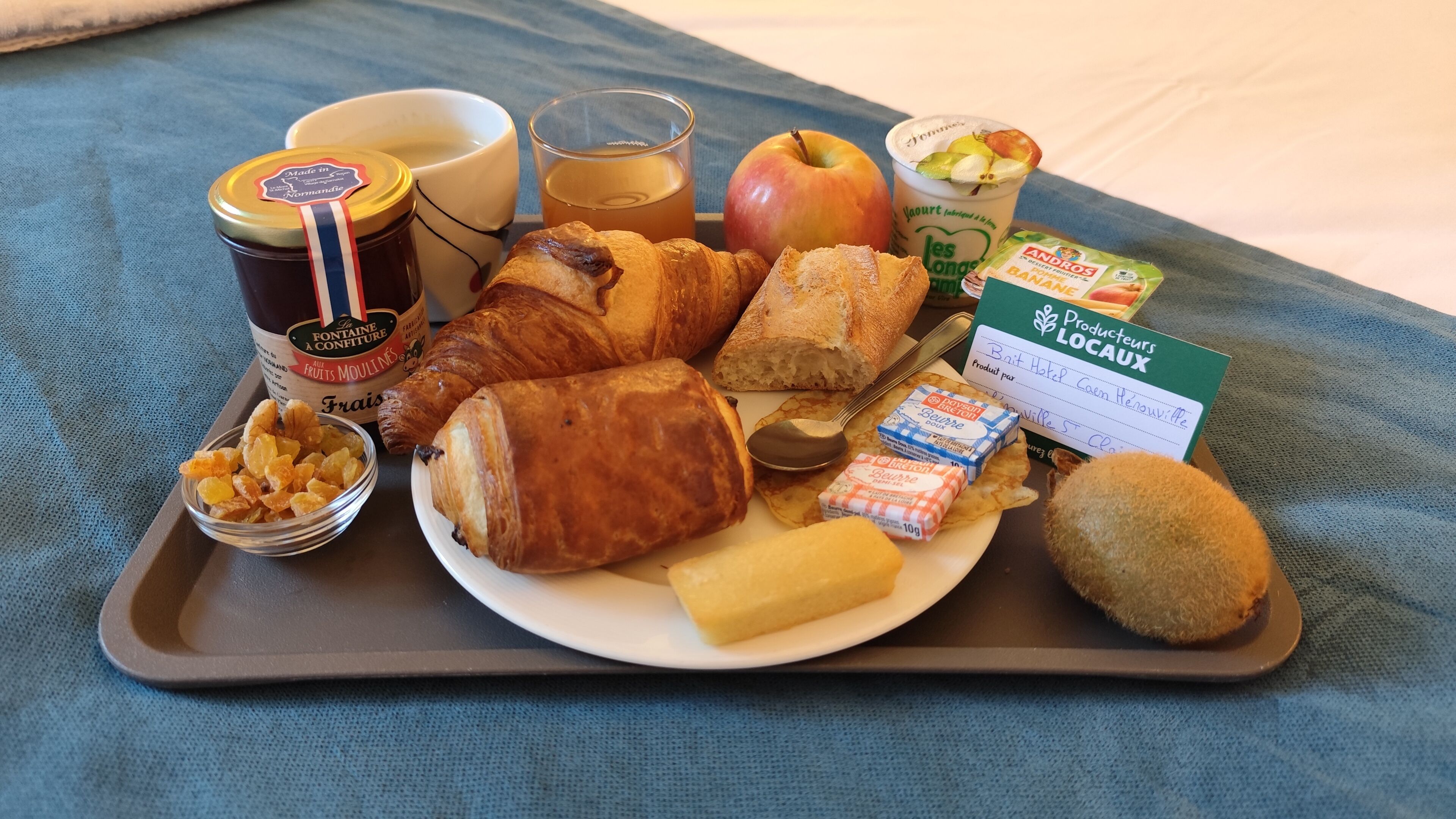 A tray with breakfast items including croissants, an apple, butter, jam, and a glass of juice.