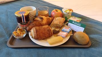 A tray with breakfast items including croissants, an apple, butter, jam, and a glass of juice.