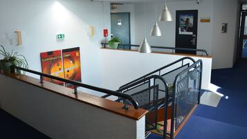 Una hall moderna di un hotel con tappeto blu, reception in legno, ringhiere metalliche e un grande poster appeso al muro.