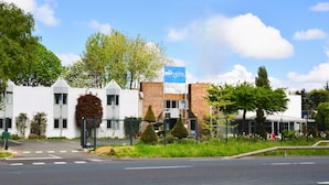 A modern hotel with a white facade, a blue sign, and a gated entrance. - Brit Hotel Caen Herouville (Herouville-Saint-Clair)