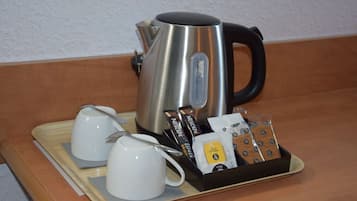 Una tetera de acero inoxidable, dos tazas blancas y una bandeja con cápsulas de café y una cuchara.