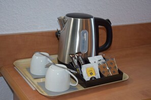 Una tetera de acero inoxidable, dos tazas blancas y una bandeja con cápsulas de café y una cuchara.