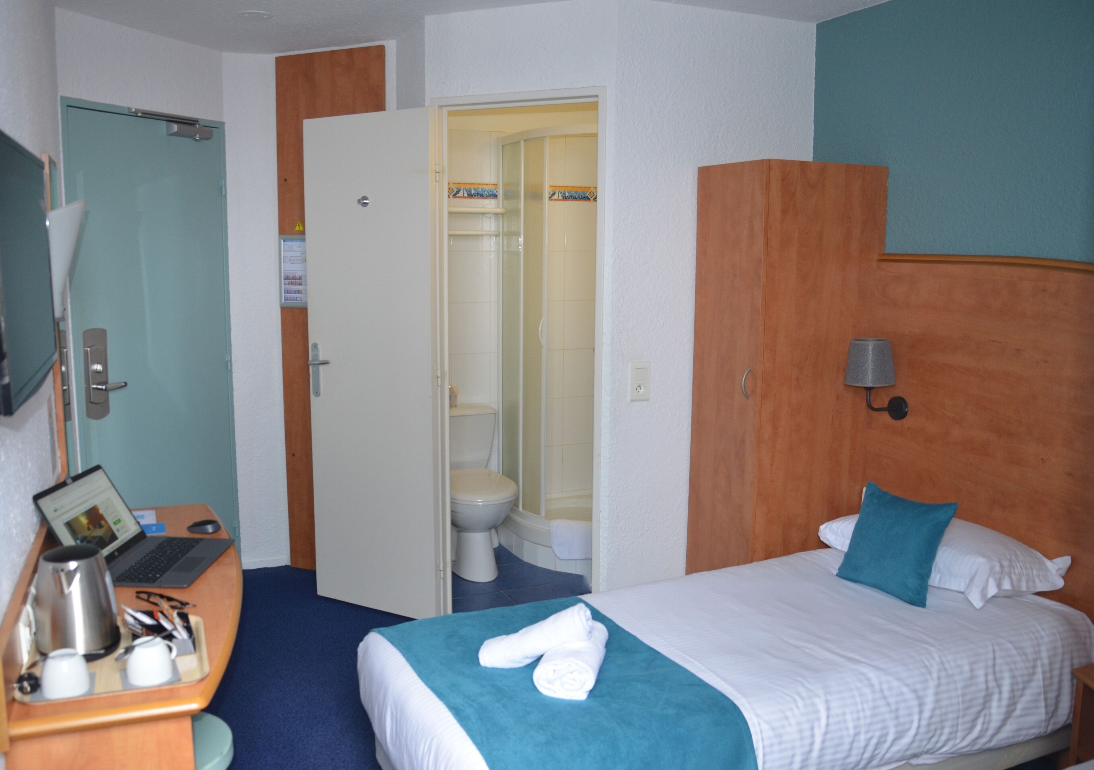 Une chambre d’hôtel équipée d’un lit, d’un bureau avec un ordinateur portable, d’une machine à café et d’un espace douche.