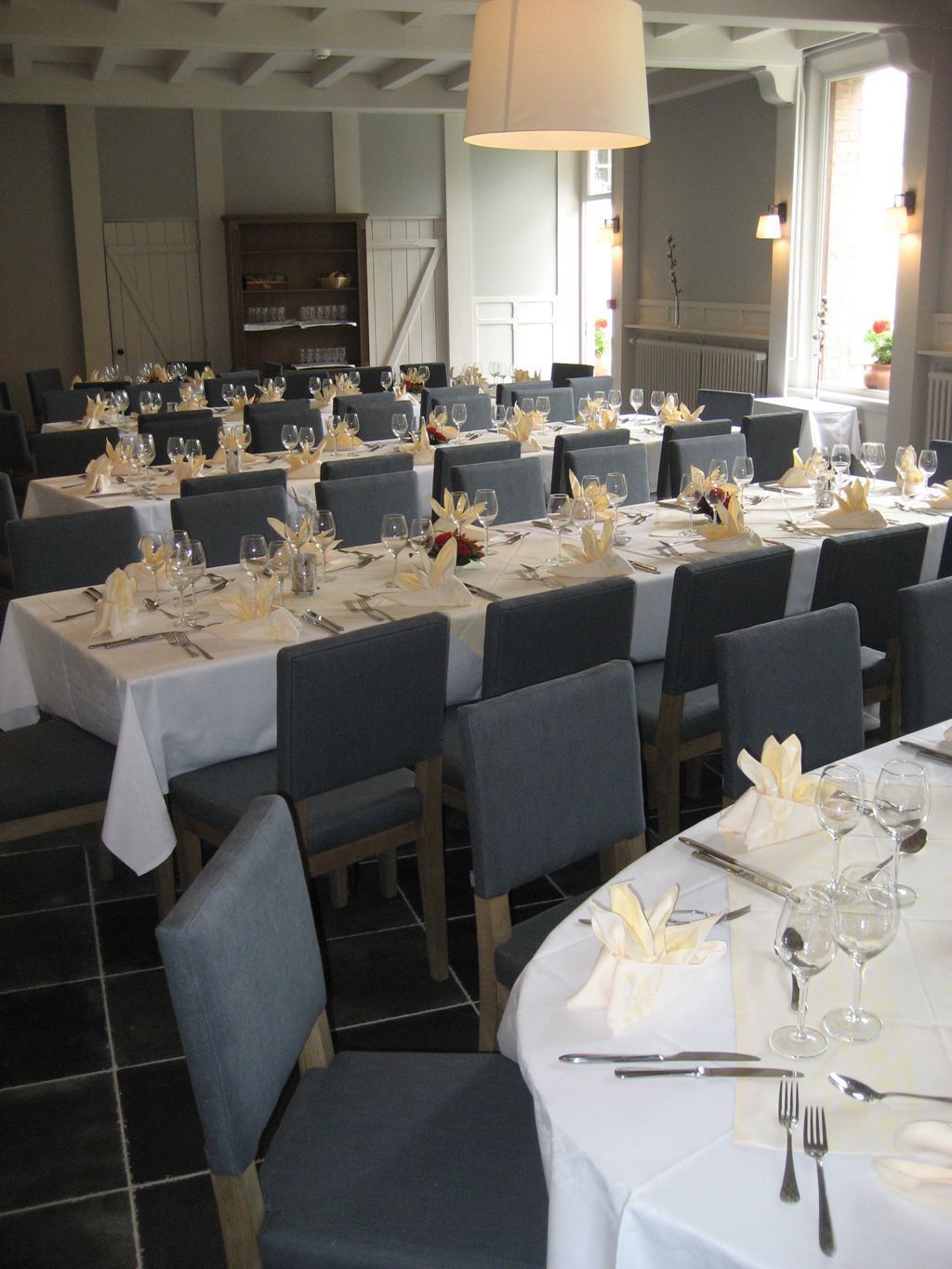Un restaurant avec de nombreuses tables dressées pour le service, avec des nappes blanches et des chaises grises.