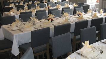 Un restaurant avec de nombreuses tables dressées pour le service, avec des nappes blanches et des chaises grises.
