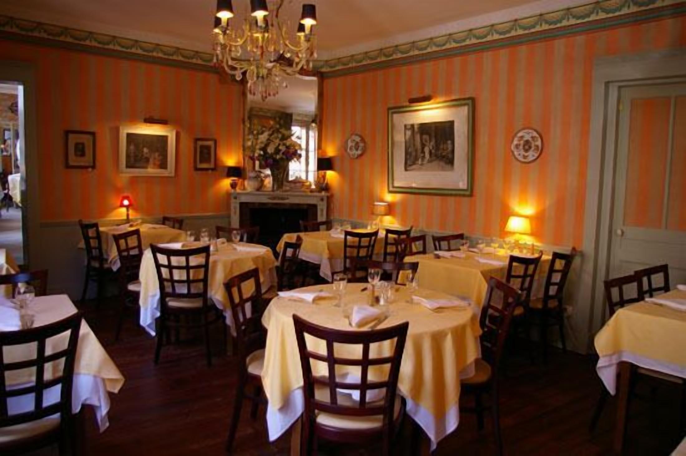 A dining area with round tables covered in yellow tablecloths, wooden chairs, and a chandelier.