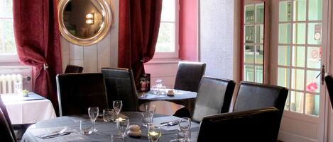 Un rincón de comedor con un espejo redondo, cortinas rojas y una mesa para dos, con copas de vino y cubiertos.