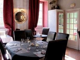 Uma sala de jantar com espelho redondo, cortinas vermelhas e mesa posta para dois, incluindo copos de vinho e talheres.