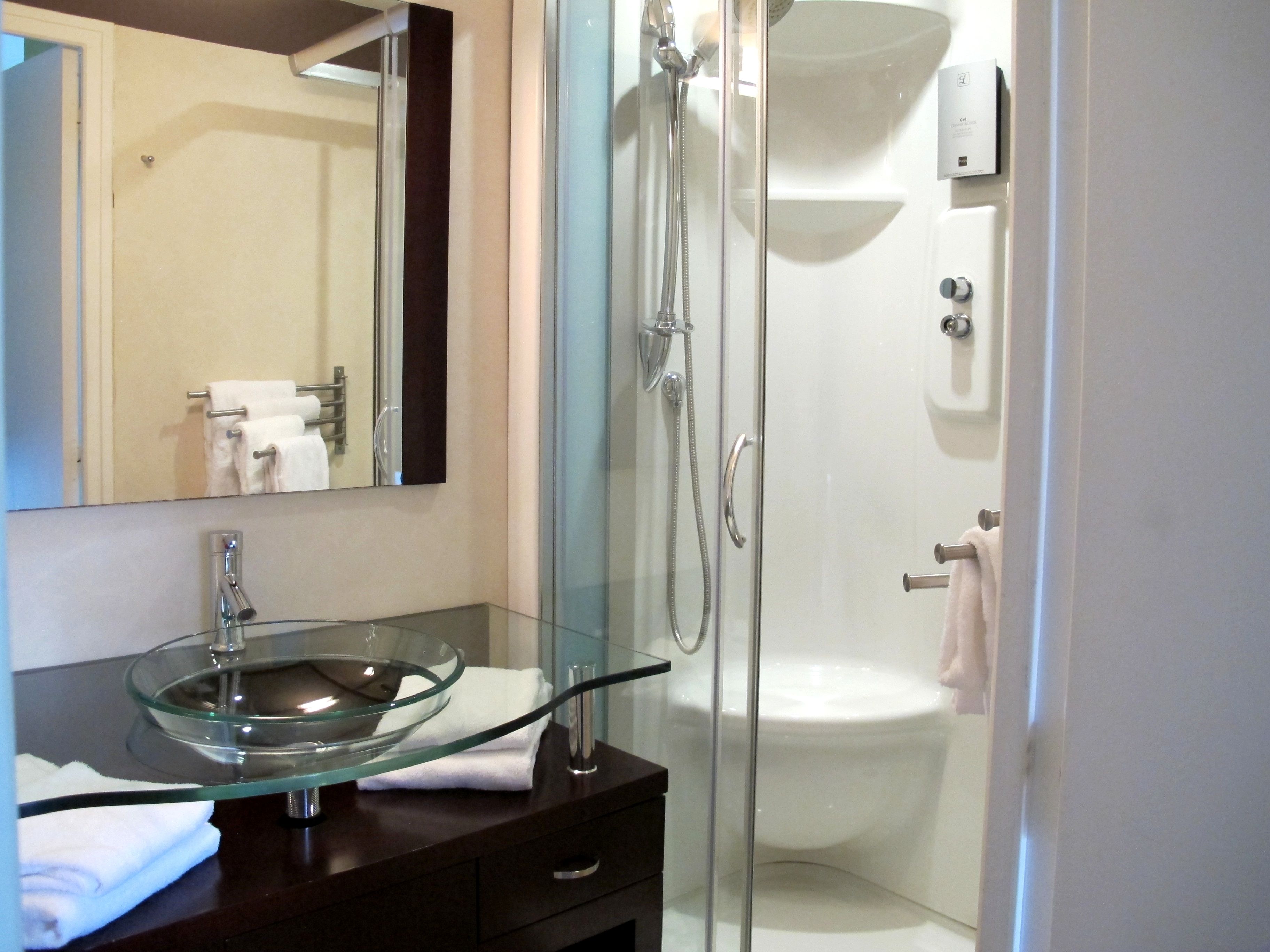 A modern bathroom with a glass bowl sink, a glass-enclosed shower, and a white toilet.