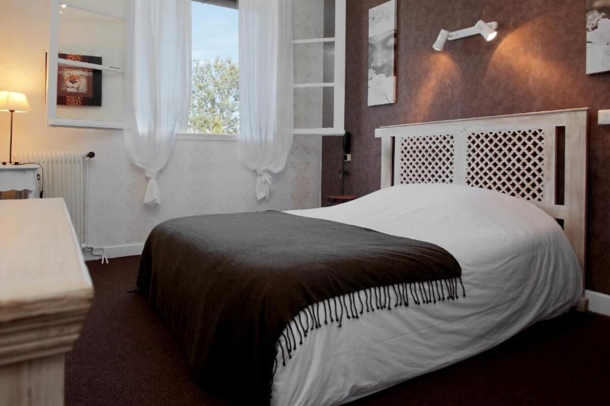 A bedroom with a bed, a bedside table, a window with curtains, a radiator, and wall art.