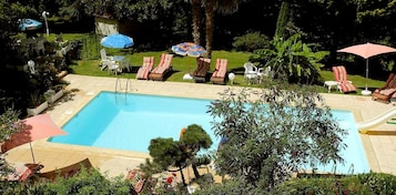 Uma piscina retangular com escorrega, rodeada por espreguiçadeiras e guarda-sóis.