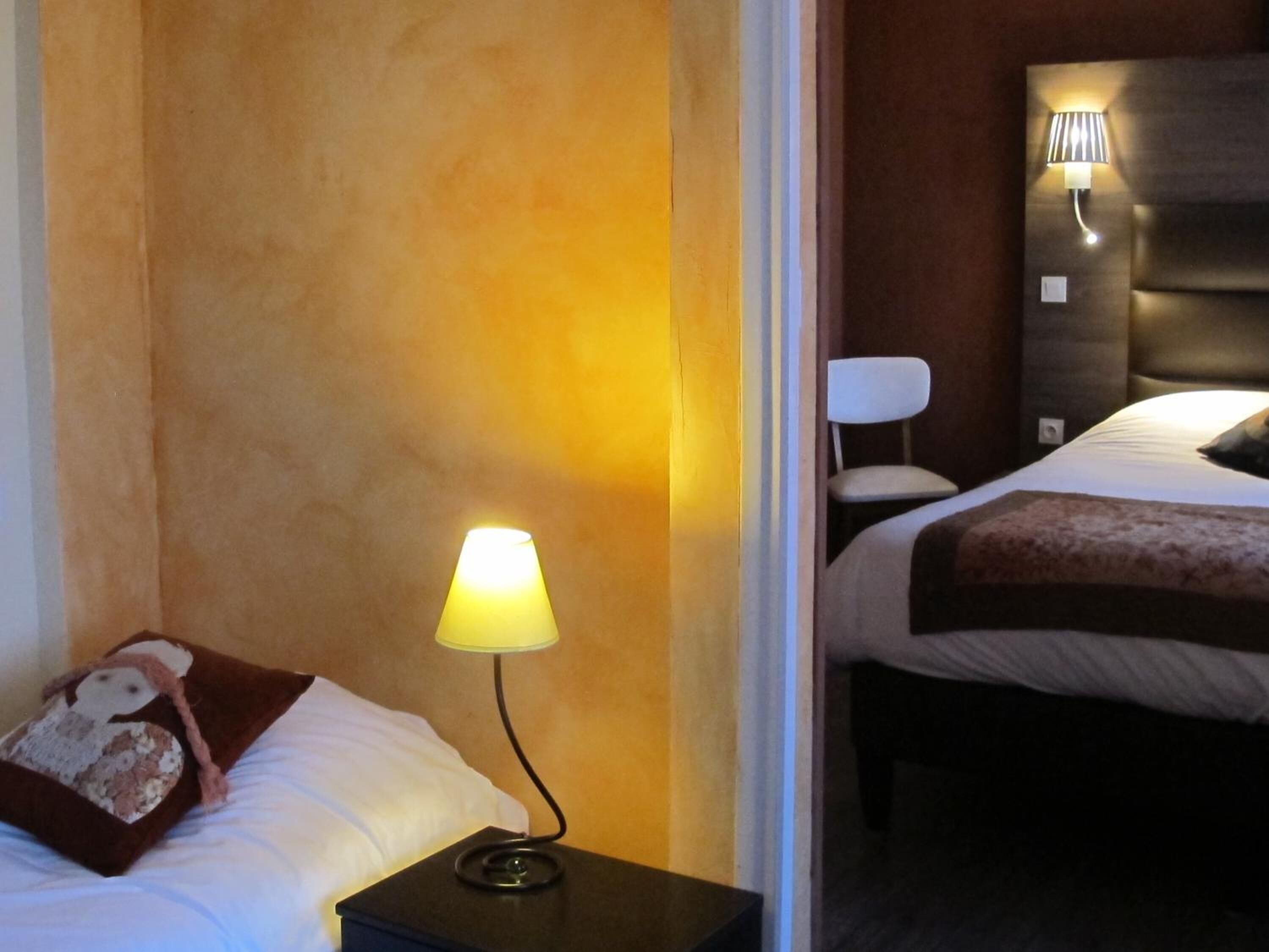 A hotel room with a bed, a nightstand with a lamp, a chair, and a wall-mounted light fixture.