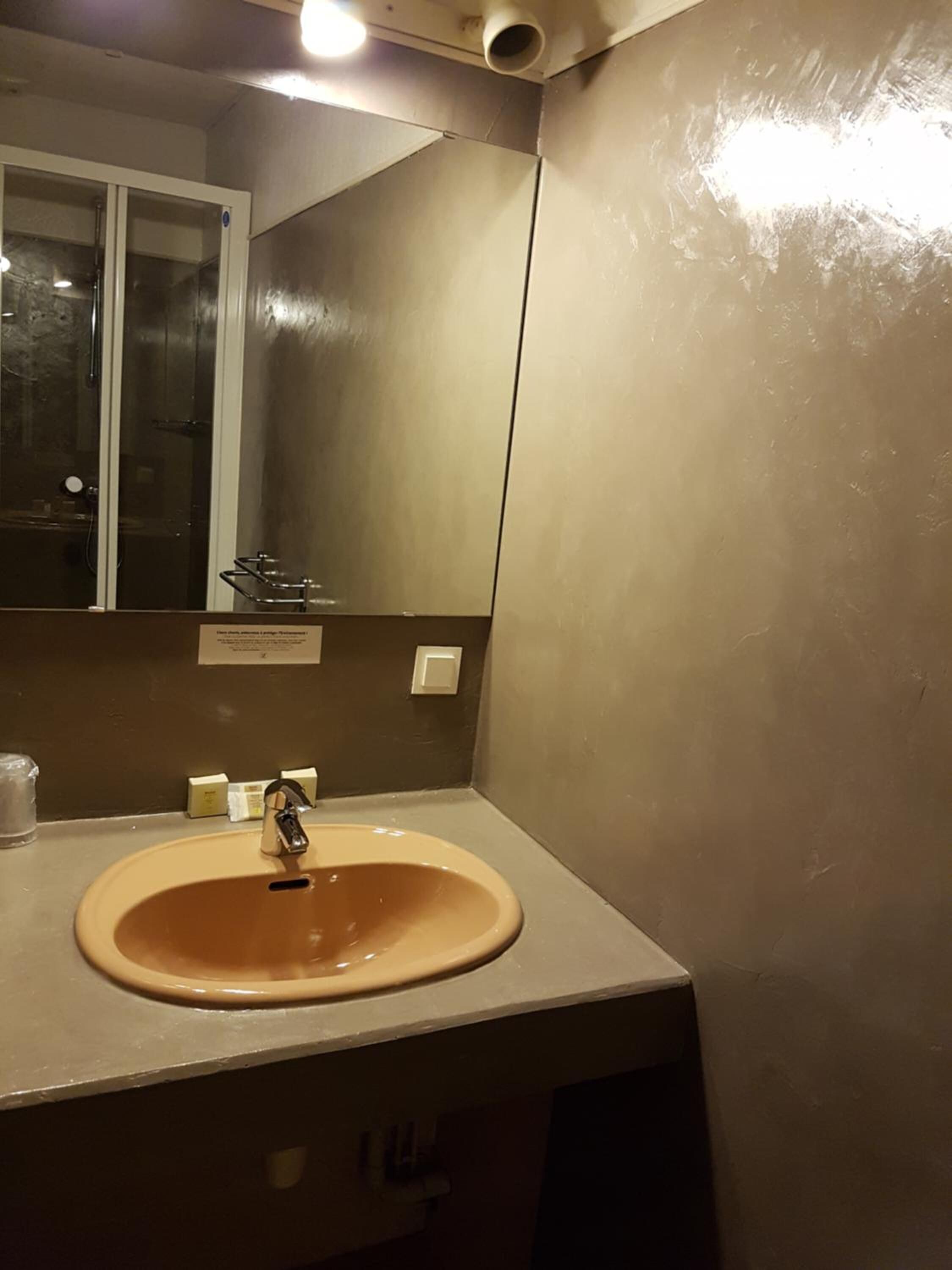 Un baño con un lavabo beige, un espejo y una cabina de ducha.